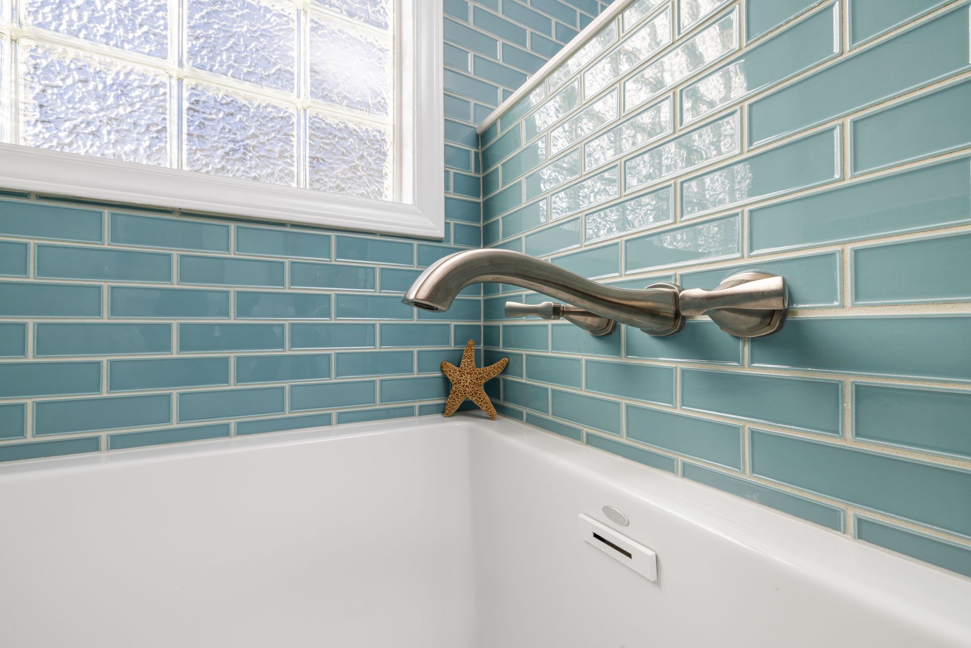 A close-up of a modern bathroom featuring a blue tiled wall and sleek faucet over a bathtub.